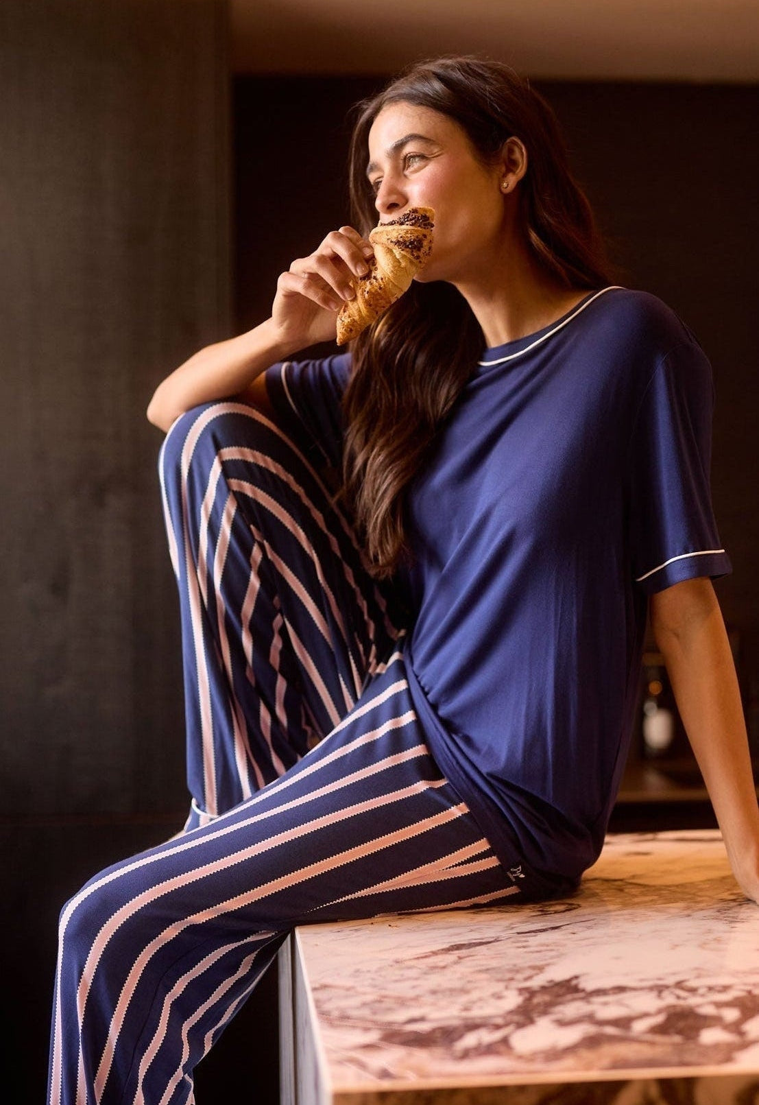 Woman in blue pajama set eating a pastry on a wooden table.