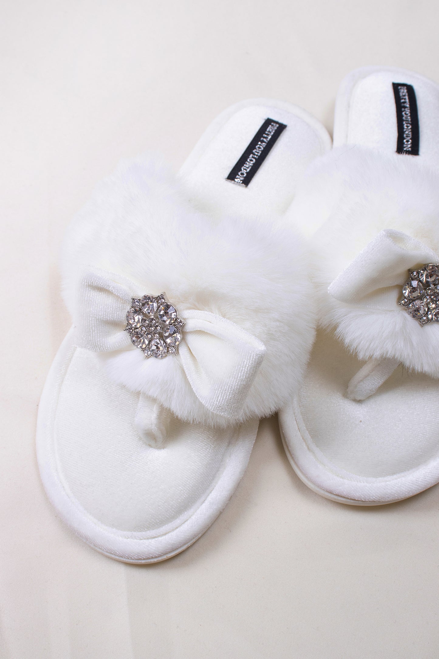 
                  
                    Amelie women's toe post slippers in cream with a premium velvet bow and diamante embellishment atop a plush faux fur band from Pretty You London
                  
                